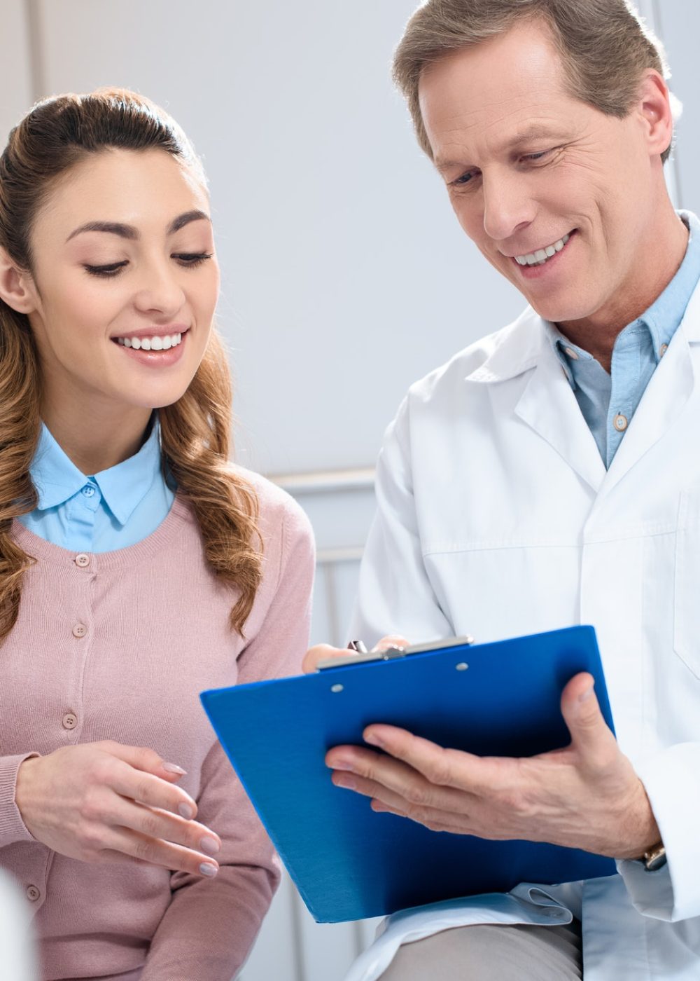 handsome-doctor-showing-something-in-clipboard-to-smiling-patient-in-clinic.jpg